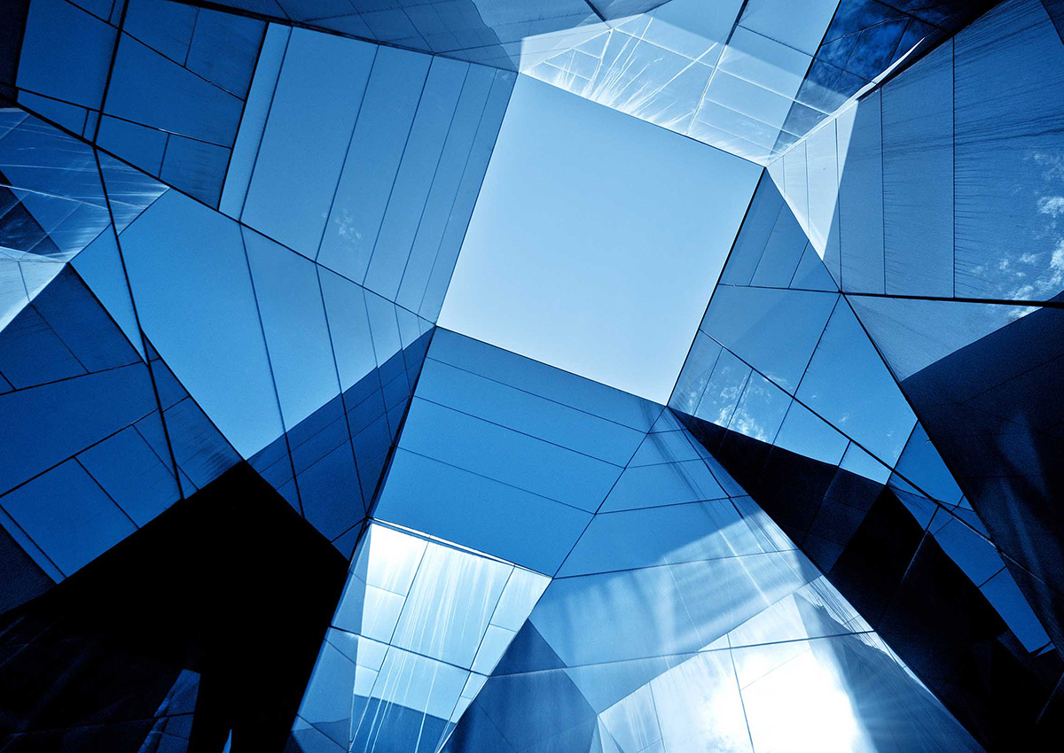 View angled up at a square skylight within a faceted glass window building facade.
