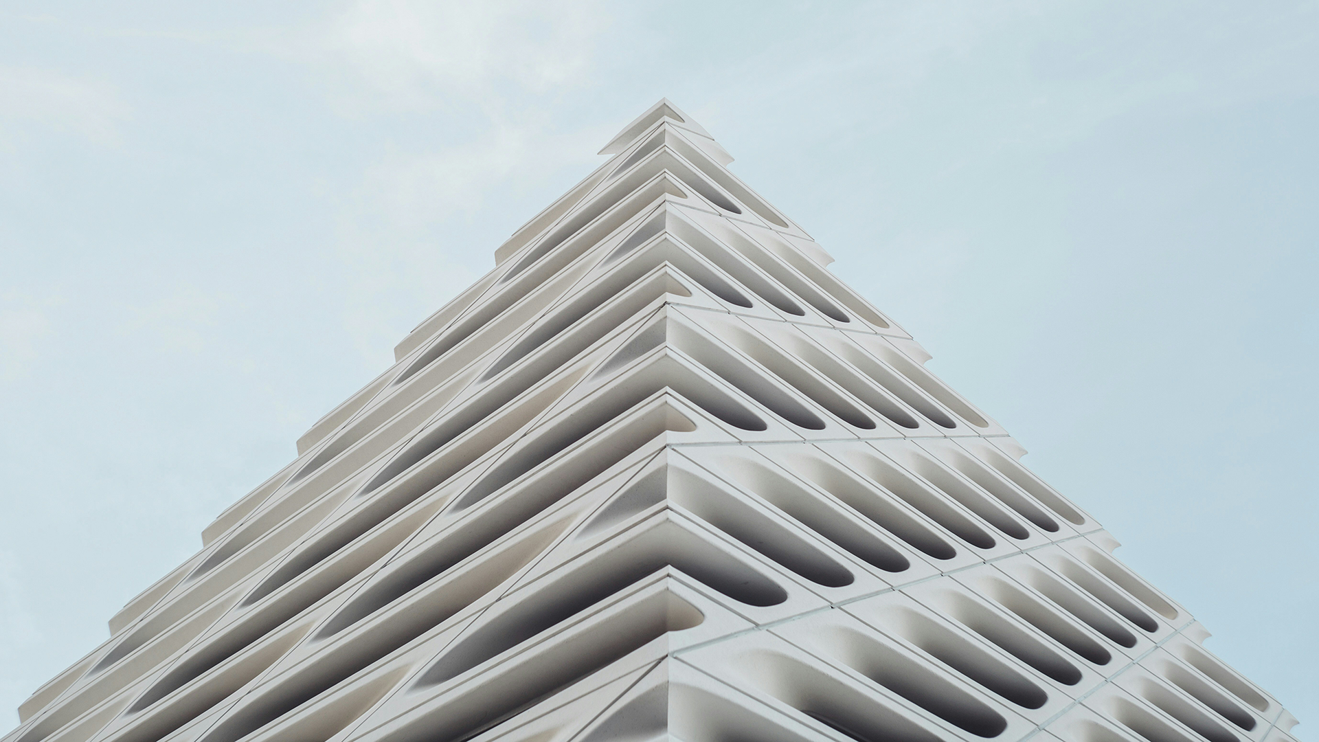A modern, uniquely designed high-rise building viewed from below against a blue sky.