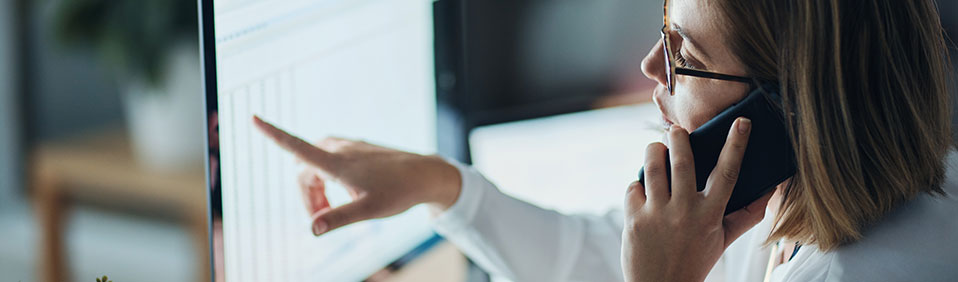 A woman working at a computer talking on the telephone.